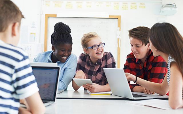 A group of teenagers are gathered together on laptops and tablets.