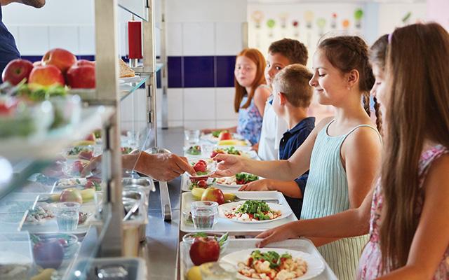 Children are lined up to collect their lunch trays at school.