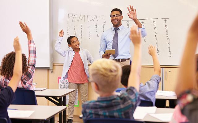 A teacher stands at the front of a math class teaching the order of operations.