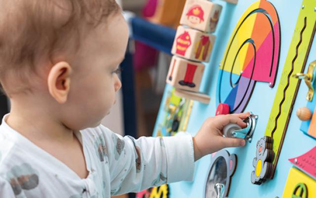 A little boy interacts cautiously with a learning board.