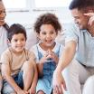 A mother, father, and two young children sit on a white couch together, smiling as they address a counselor.