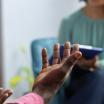 A counselor in a turquoise shirt holds a tablet and speaks with their patient, a man with dark skin and a pink shirt. Neither of their faces are visible.