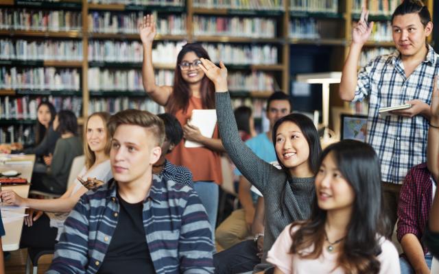 Students raising their hands in a library