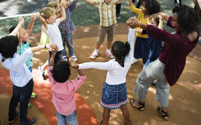 Elementary school children playing with their teacher outdoors.