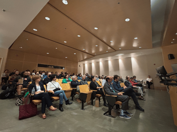 A crowd of people look toward the front of a large lecture hall.