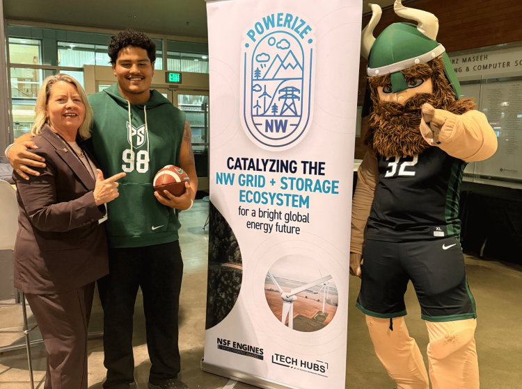 A woman in a suit, a young man holding a football, and a viking mascot pose in front of a sign for Powerize NW.