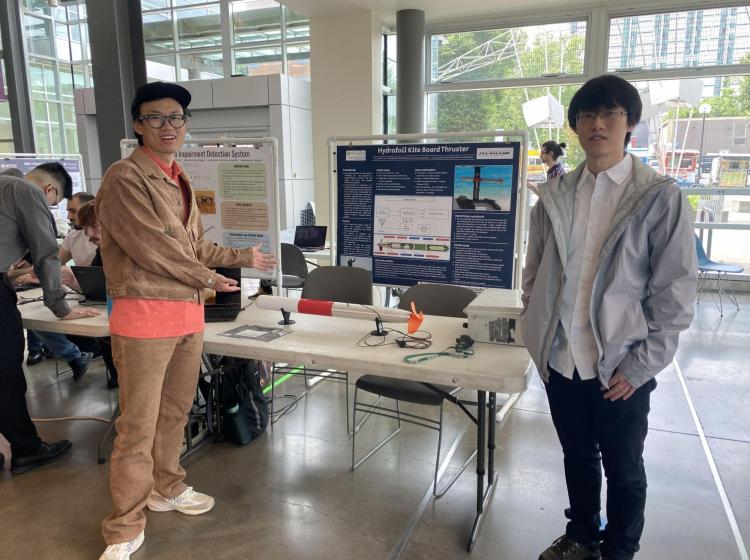 Two students standing at a table presenting their project at a university event.