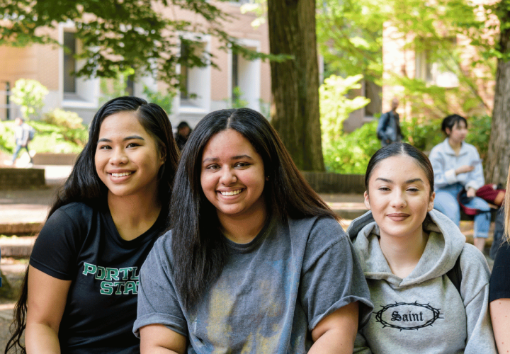 Four young people pose sitting outside in the park blocks.