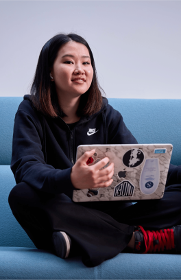A young woman holds a laptop covered in stickers on a couch.