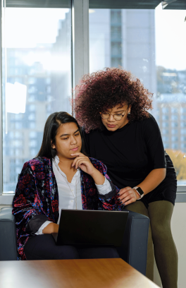 Two people wearing fashionable clothes look at a laptop.
