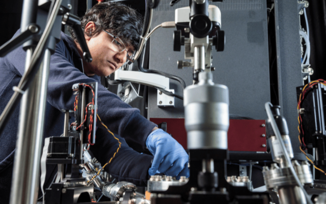 A person wearing plastic gloves works with a complicated machine.
