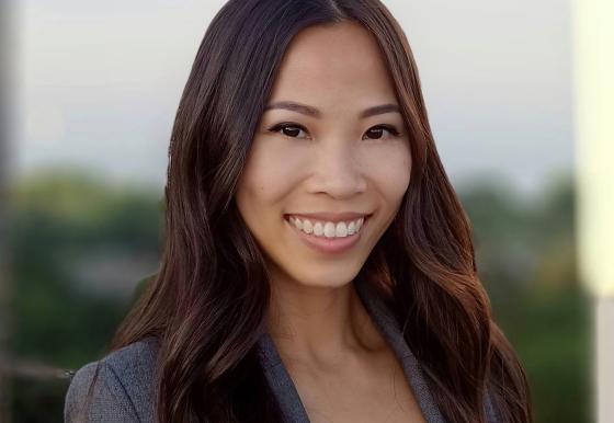 A professional-looking woman wearing a gray blazer smiles broadly. 