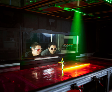 Two people wearing sunglasses look at a laser and miniature mind turbine.