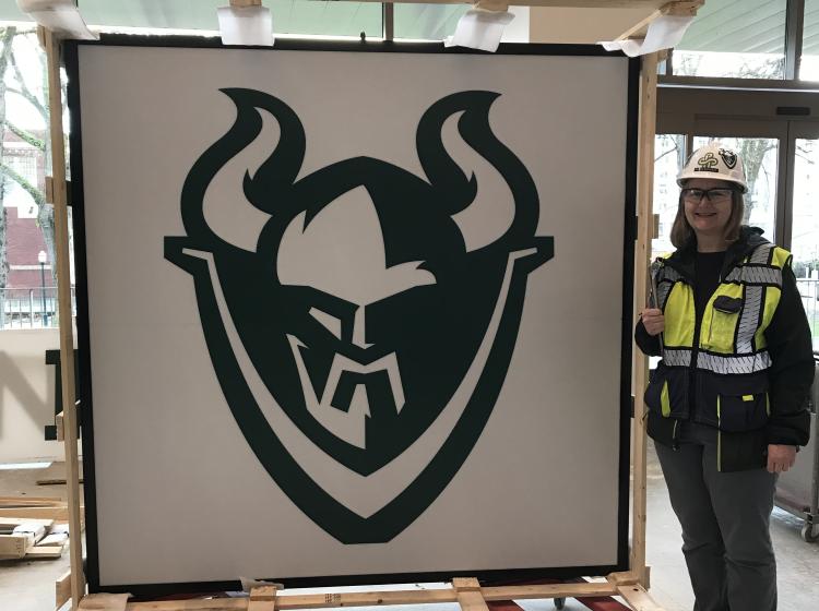 A woman in PPE next to a sport's sign that has been taken down