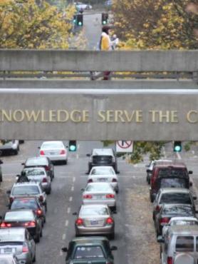 Cars on the road driving under a foot bridge that reads "Let Knowledge serve the city"