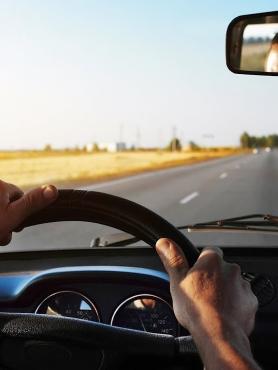 Two hands on a sterring wheel with a view of open road in front