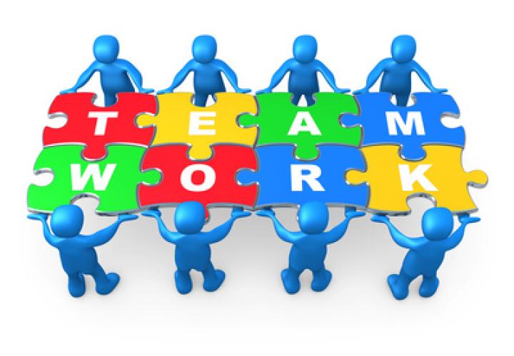 Individuals around a table made up of puzzle pieces, which spell out teamwork