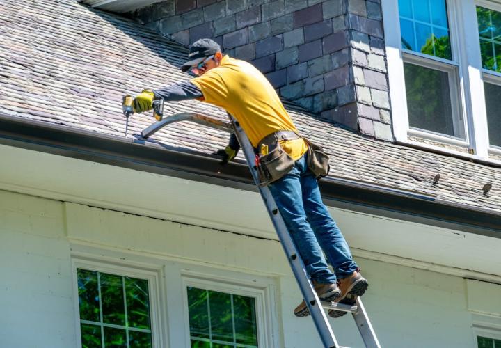 man using tool on ladder while working on roof