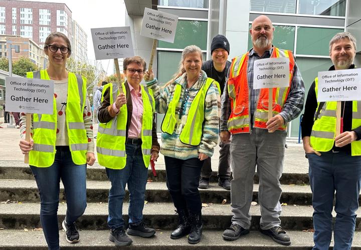 Group of fire safety monitors wearing safety vests and holding assembly signage