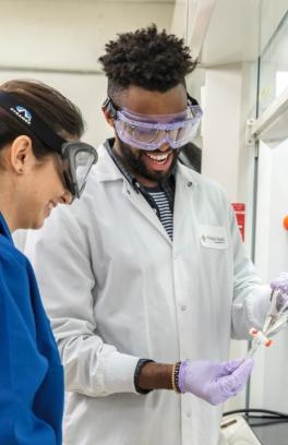 Image is of a man holding a piece of scientific equipment and showing it to a colleague