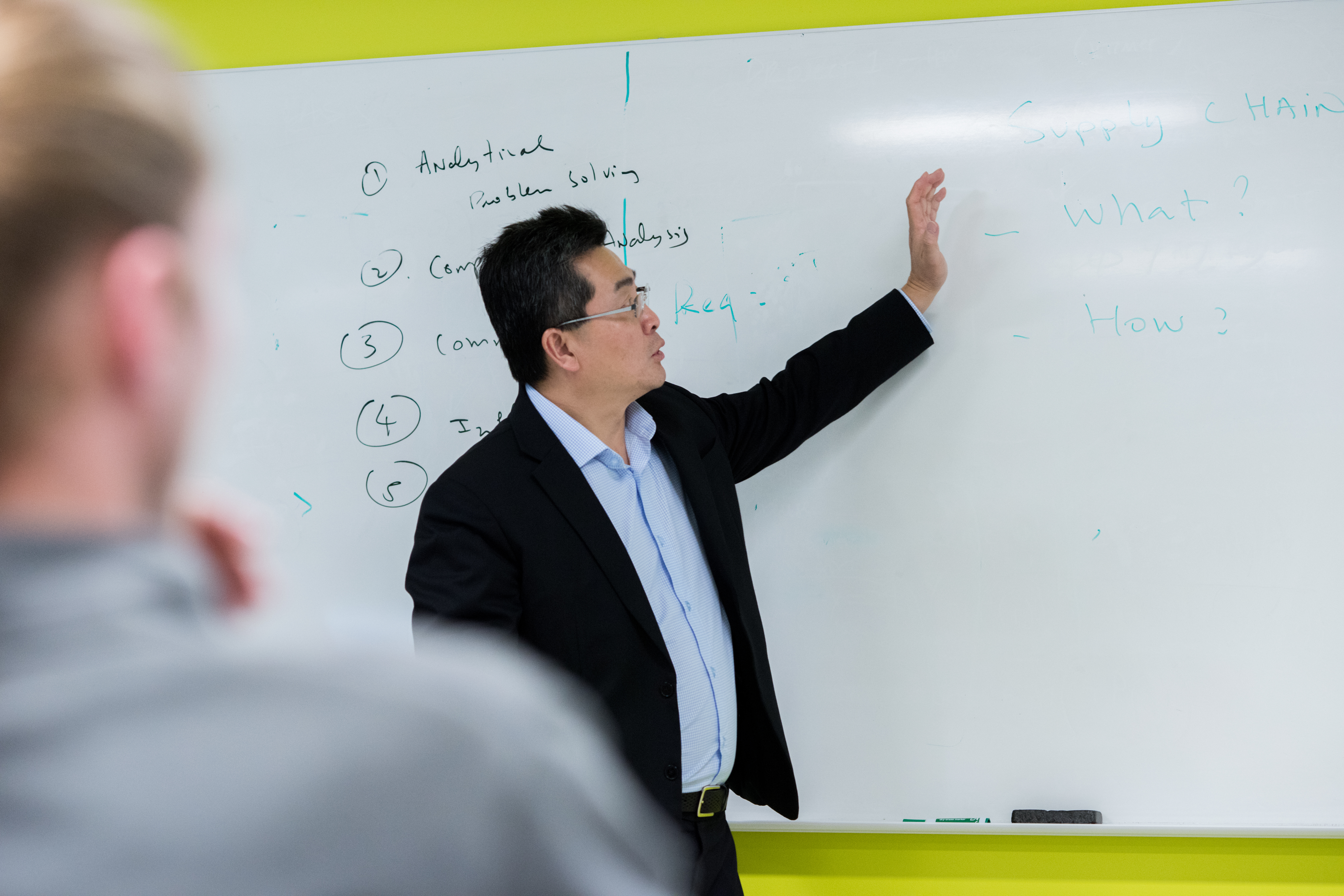 Faculty stands at whiteboard, pointing