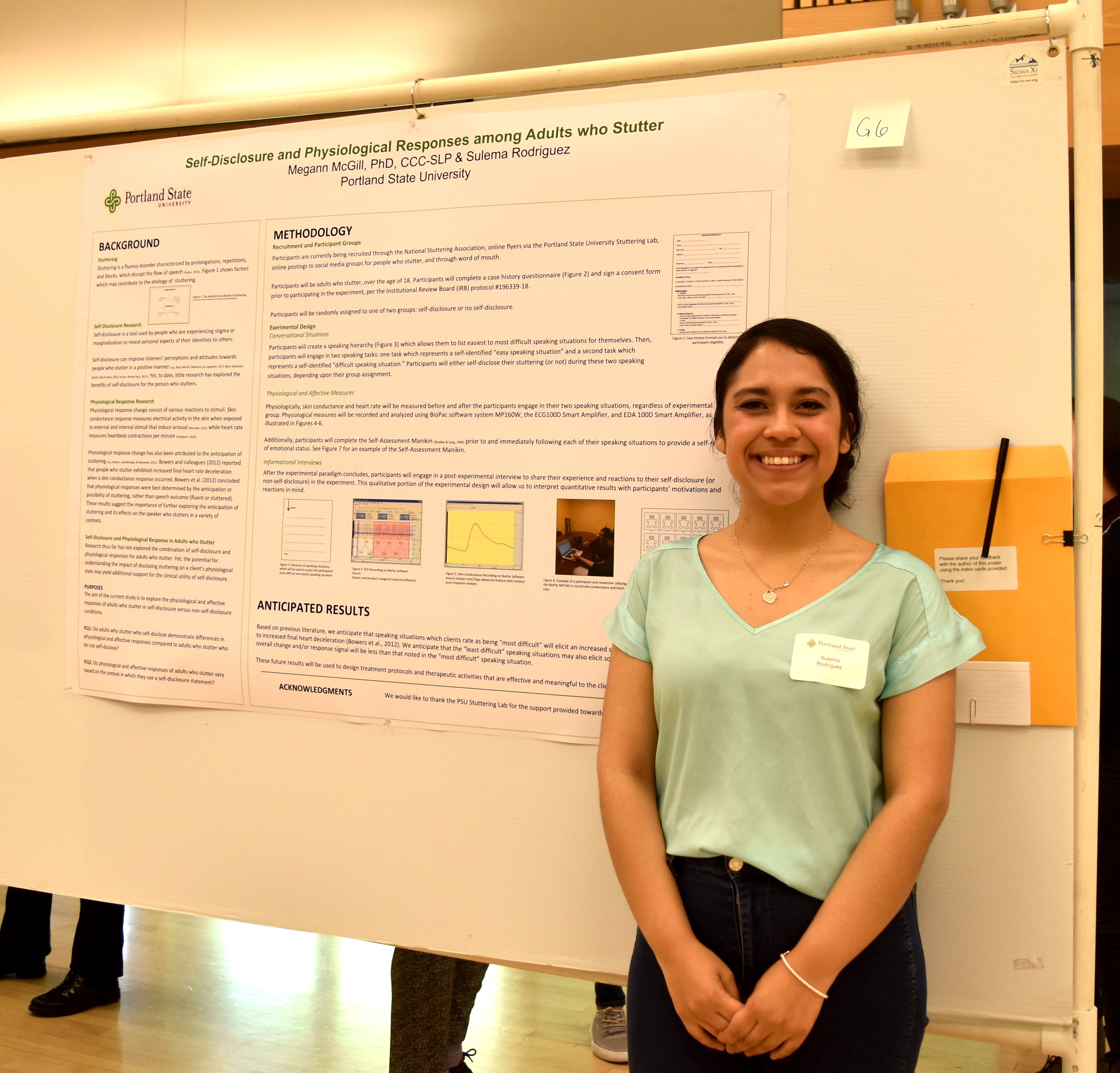 A student stands smiling in front of their research poster