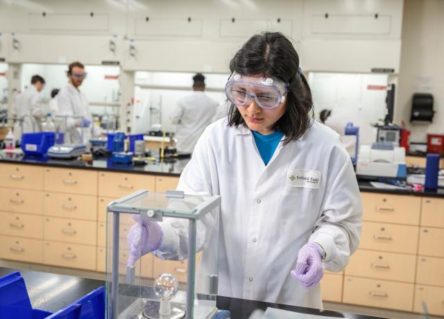 a student wearing a lab coat and goggles performs some sort of experiment in a bench lab 