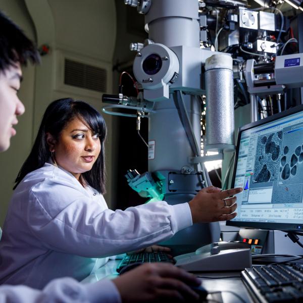 a faculty points to something on a screen in a bench science setting and student looks on