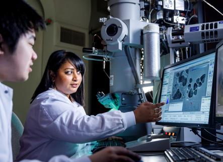 a faculty points to something on a screen in a bench science setting and student looks on