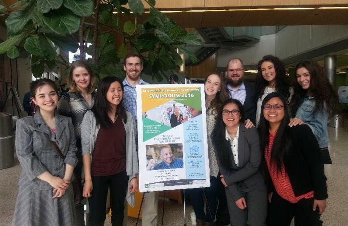 9 students and faculty stand next to a poster