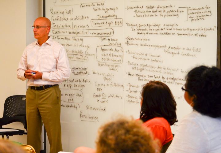 Faculty in front of white board with students in a classroom