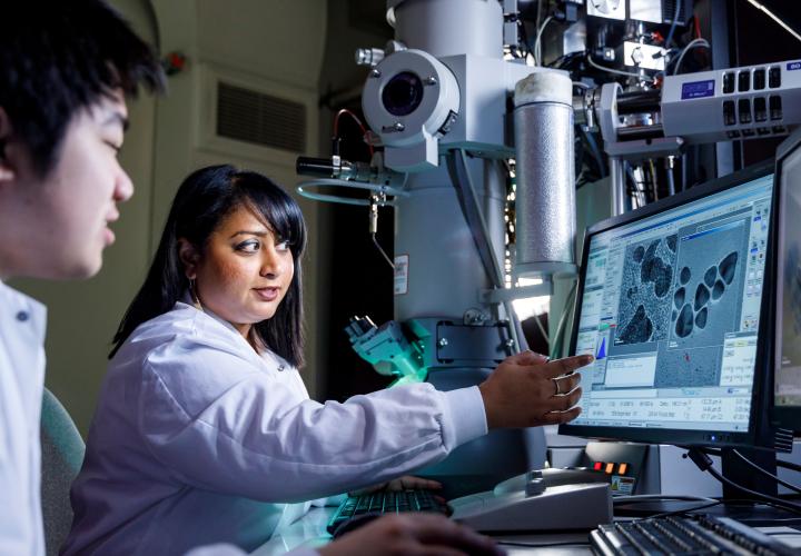a faculty points to something on a screen in a bench science setting and student looks on