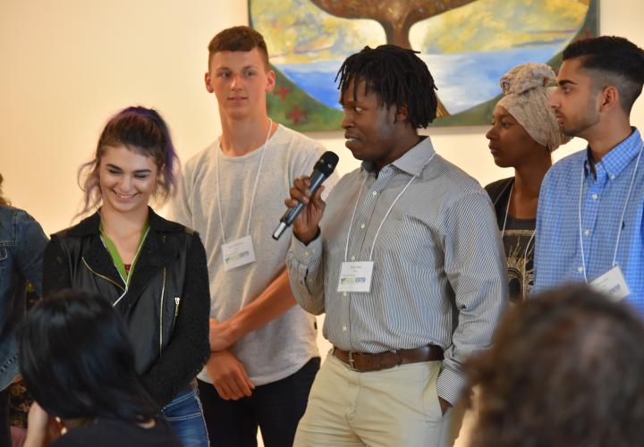 A student stands with the mic in hand while a small group of other students stand with them.