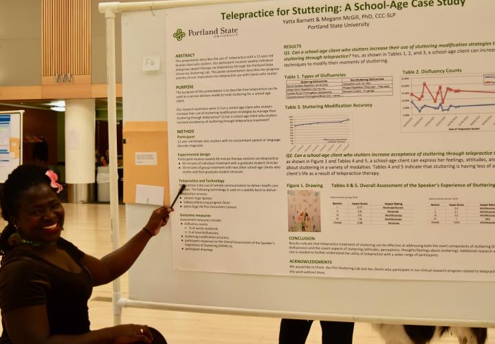 A student sits next to a scientific poster and points to it.