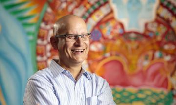 Faculty member Carlos Crespo stands in front of a colorful mural