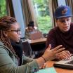 two students sit at computer engaged in conversation