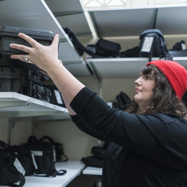 Student worker shelving camera in equipment room