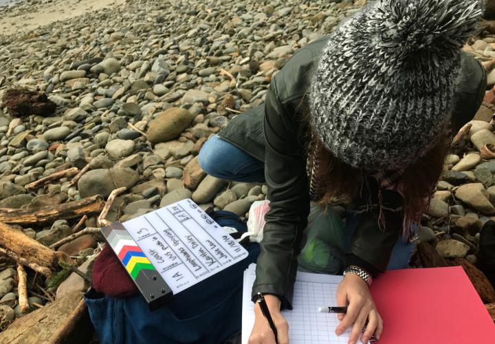 Student writing in notebook on rocky beach