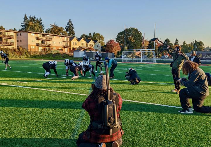 Football team sets up for a play while student in the foreground films the action