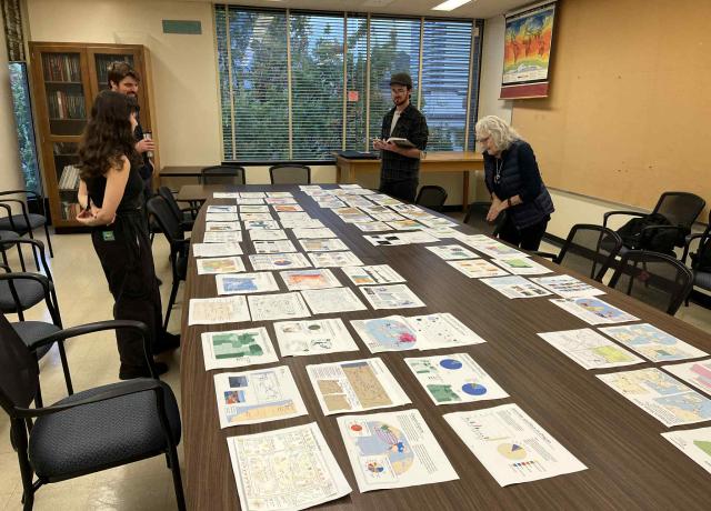 Image of a group of people at work on the pages of the Student Atlas of Oregon, which are spread across a long table.