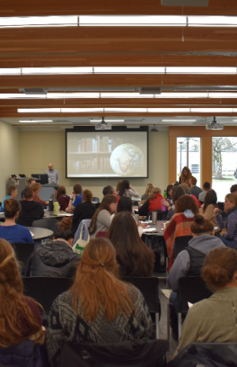 View from back of room of large audience viewing presentation screen featuring a globe