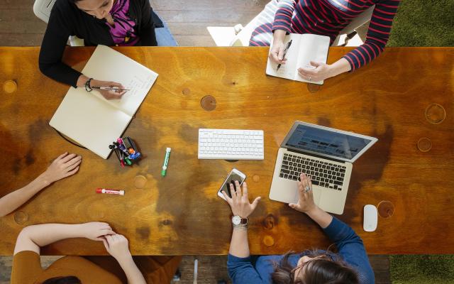 Photo of hands resting on a table with laptop and notepads