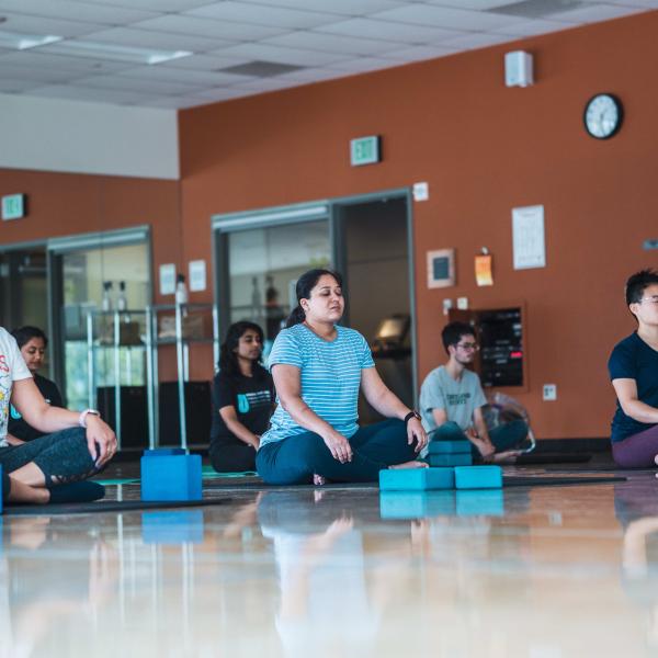 Campus Recreation - inclusive yoga and mediation in a group room. students sitting on the floor spaces out with yoga mats and stretching blocks.