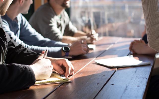 This photo is decorative. A group of students talking at a table with forms and notebooks.