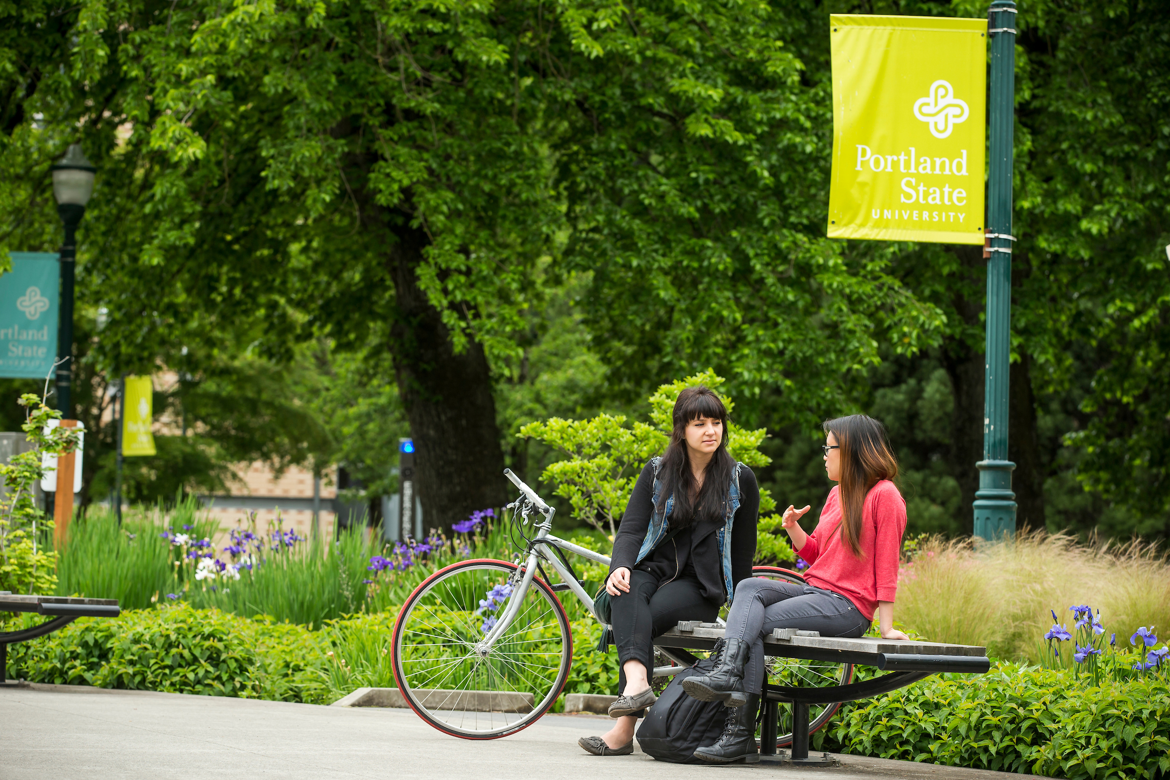 Two women conversing on bench, one has bike next to her