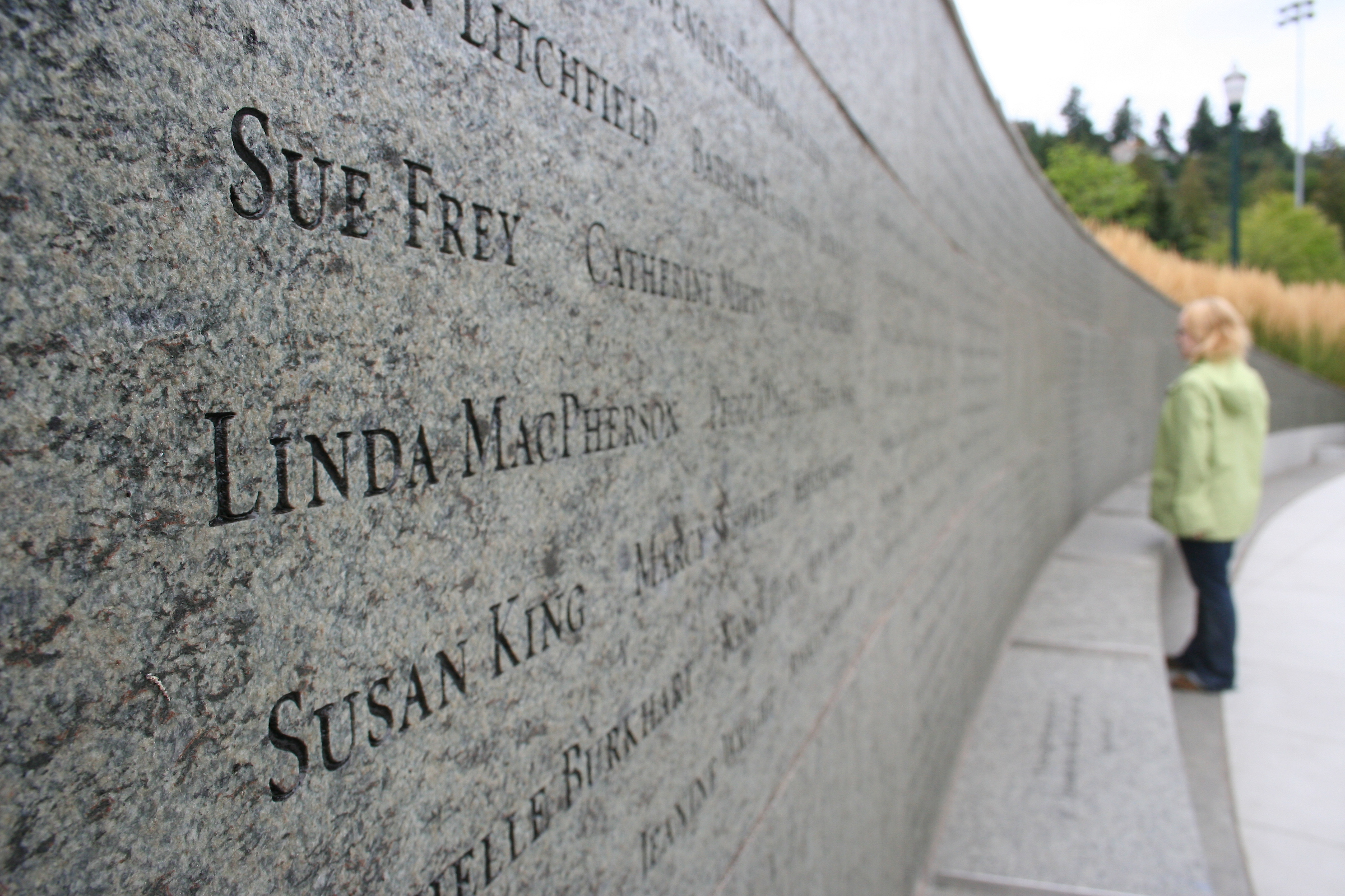 Close up of stone wall with engraved names and woman in background