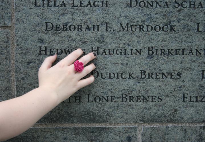 Close up of hand touching engraved names on stone wall