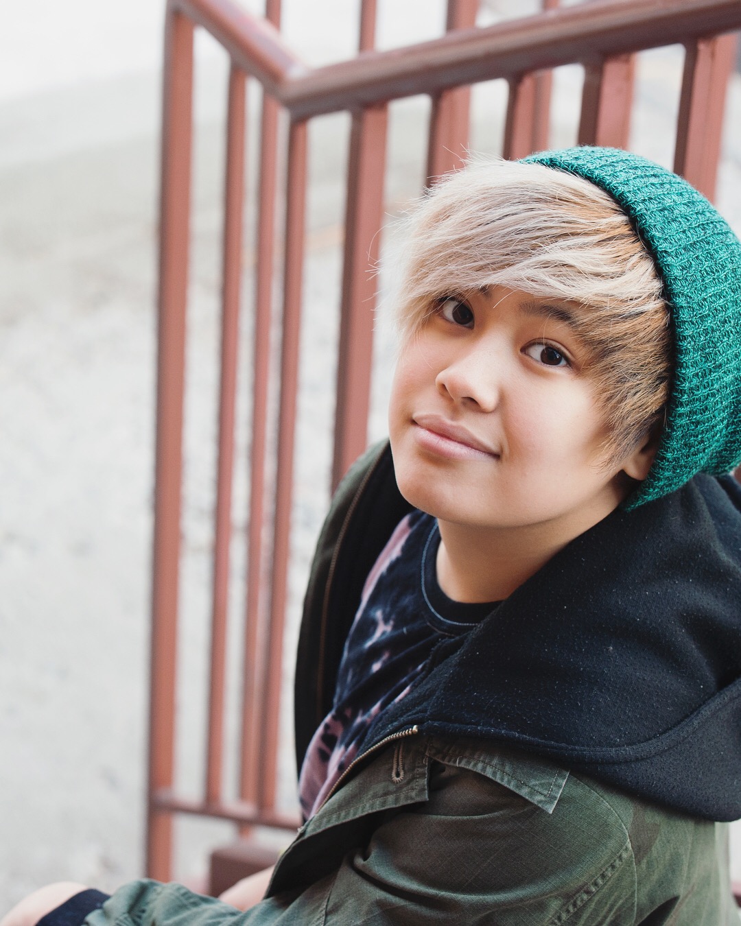 Photo of Shaun Hardy, who is sitting on some stairs and looking up at the camera, wearing a teal hoodie.