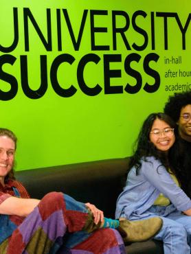 Three students sitting in front of green wall that reads University Success