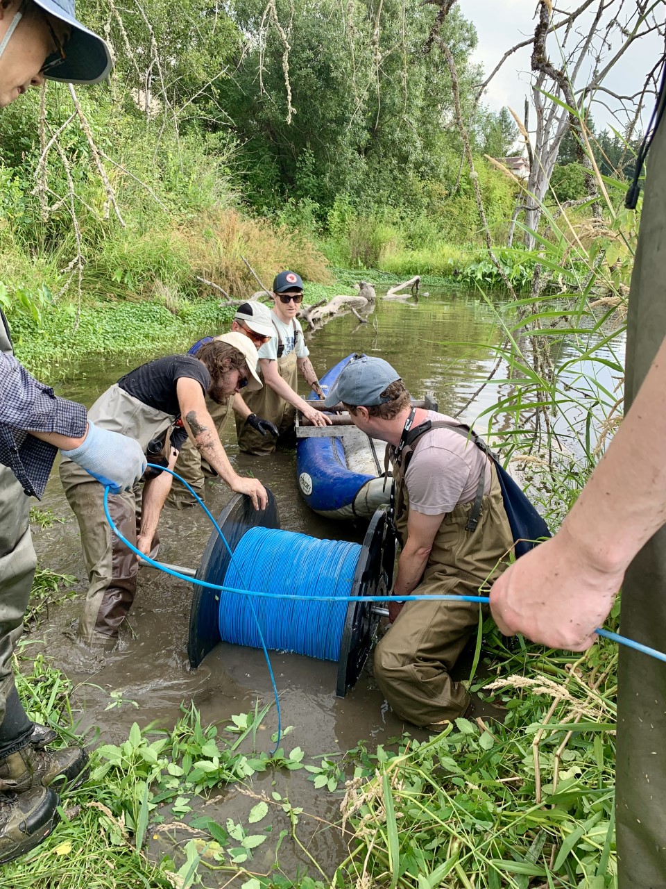 Researchers are setting up water temperature equipment, a long blue cable, in a stream